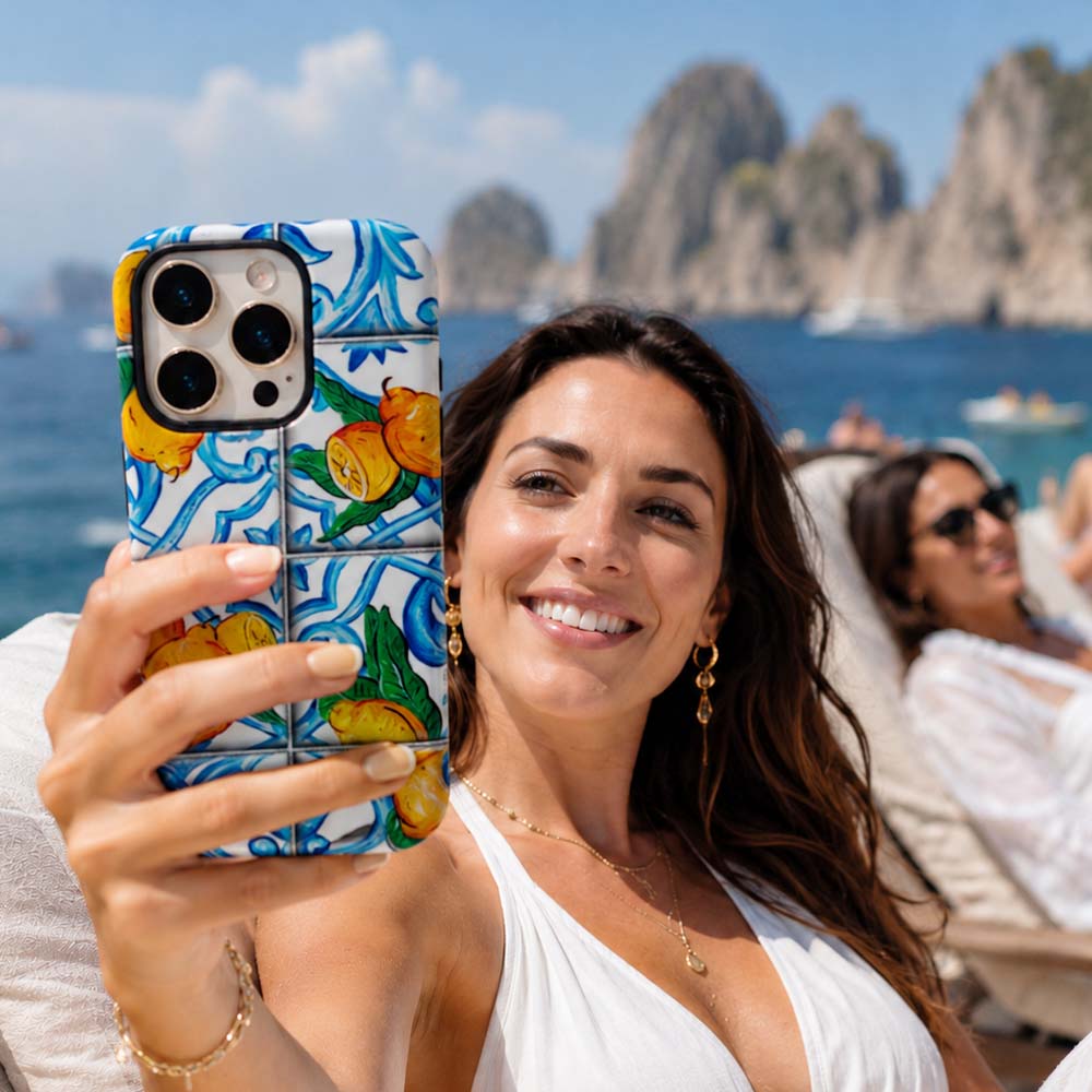 Woman on luxury boat holds up pretty lemon phone case with Italian majolica tile design and lemons