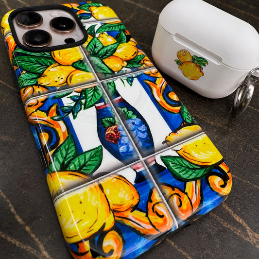 A close-up of a phone case with a colorful mosaic tile pattern featuring lemons, green leaves, shown next to a white AirPods case on a dark textured surface.