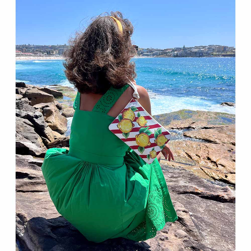 Model wears lemon and red white stripes bag by DOLCE ITALIANA overlooking beach in Australia